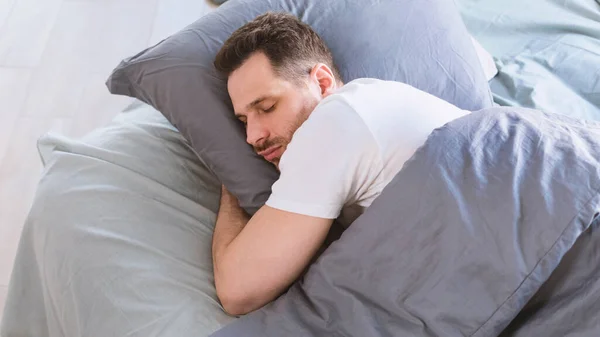 Bărbat dormind îmbrățișare pernă culcat în pat odihnindu-se în dormitor — Fotografie, imagine de stoc