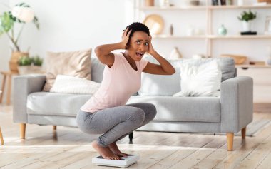 Şok olmuş siyah kadın terazide oturuyor ve evdeki aşırı ağırlık yüzünden kafasını koparıyor.