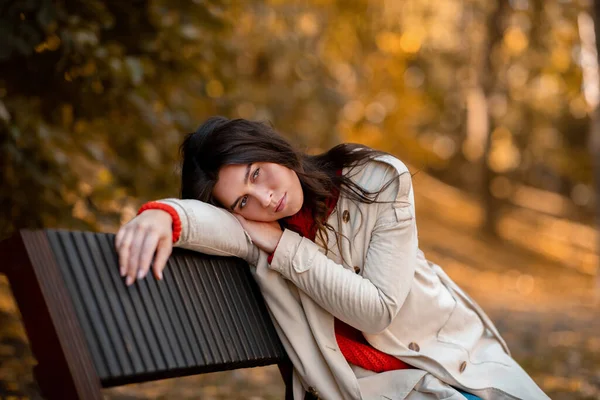 Wanita muda yang tidak bahagia dengan pakaian kasual duduk di bangku cadangan di taman musim gugur — Stok Foto
