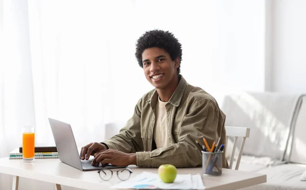 Conceito de educação remota. Preto adolescente cara digitando no computador portátil durante seus estudos on-line em casa — Fotografia de Stock