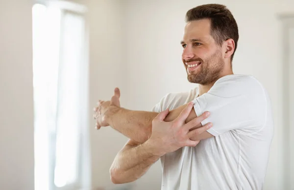 Hombre feliz entrenando en casa, ejercitando los brazos extendidos en el dormitorio —  Fotos de Stock