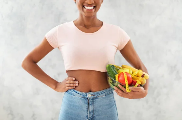 Närbild bild av ung afroamerikansk kvinna som håller färska frukter och grönsaker med måttband på grå bakgrund — Stockfoto