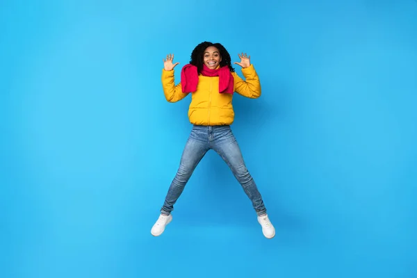 Alegre mulher africana saltando mãos ondulando no meio do ar, fundo azul — Fotografia de Stock