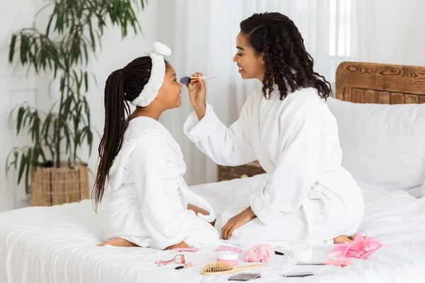 Kochająca młoda czarna matka robi makijaż swojej małej córce w domu — Zdjęcie stockowe