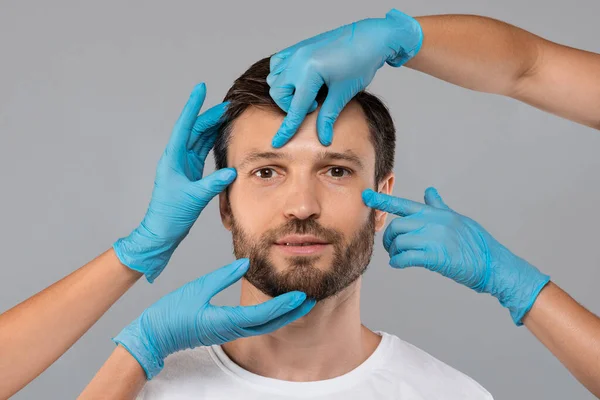 Les médecins mains dans des gants de protection touchant le visage de l'homme d'âge moyen — Photo