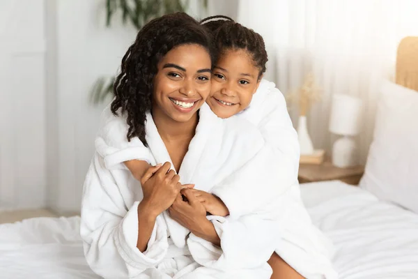 Home Retrato de feliz mãe negra e filha vestindo roupões de banho e abraços — Fotografia de Stock