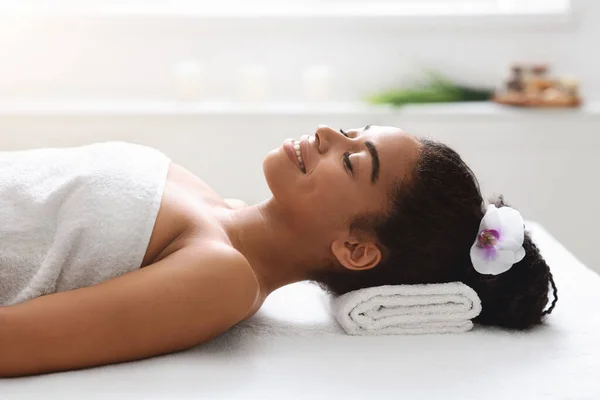 Mulher negra alegre com flor no cabelo sorrindo no spa — Fotografia de Stock