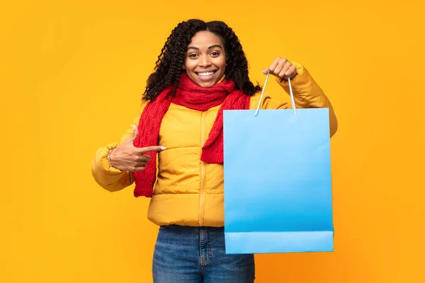Весела африканка вказує пальцем на сумку для покупок, жовтий фон — стокове фото