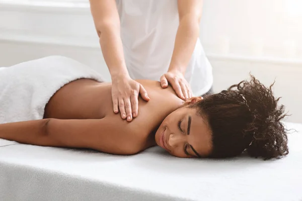 Terapeuta feminina esfregando dormindo afro-americano senhora de volta — Fotografia de Stock