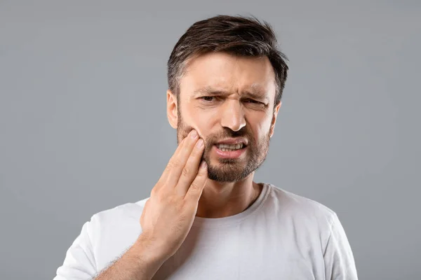 Man suffering from strong tooth pain, grey background — Stock Photo, Image