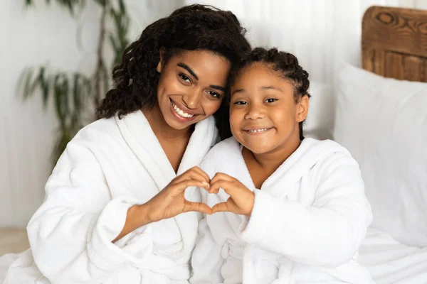 Happy Black Mom And Daughter In Bathrobes Making Heart Sign Form Hands