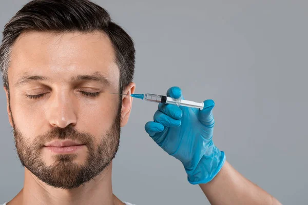 Бородатий чоловік середнього віку отримує ін'єкції проти зморшок в зоні очей — стокове фото