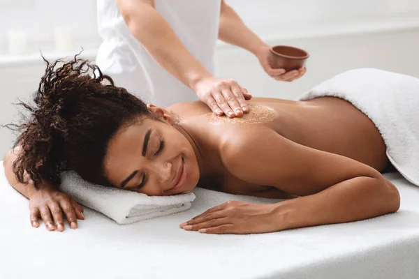 Terapeuta Spa aplicando máscara esfoliante no corpo da mulher negra — Fotografia de Stock