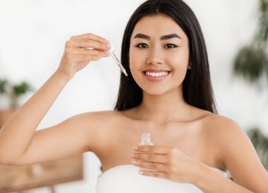Mutlu Asyalı kadın, yüz sıvısı serumu gösteriyor.