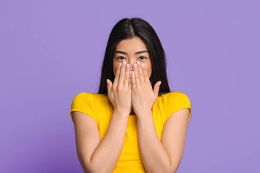 Mutlu Heyecanlar. Neşeli esmer kadın, içtenlikle gülümsüyor ve elleriyle ağzını kapatıyor, hoş bir Surprize layık görüldü, olumlu duygulara sahip, Mor Stüdyo Arkaplanı 'nın başında duruyor,