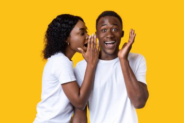 Siyahi kadın, hayret içindeki erkek arkadaşına bir şeyler fısıldıyor.