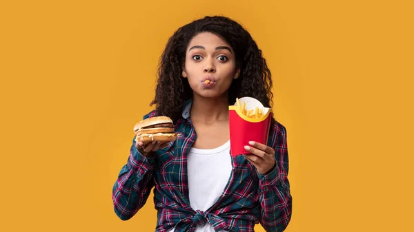 Divertida mujer afroamericana comiendo hamburguesa y papas fritas — Foto de Stock