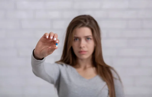 Deprimida moça mostrando antidepressivo ou sedativo comprimido contra parede de tijolo branco, foco seletivo. Espaço de cópia — Fotografia de Stock