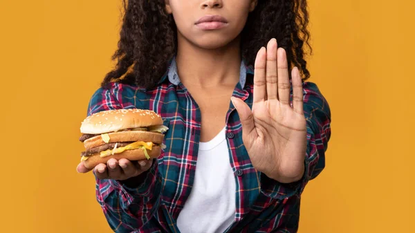 Negro dama sosteniendo hamburguesa y mostrando dejar de gesto a la cámara — Foto de Stock