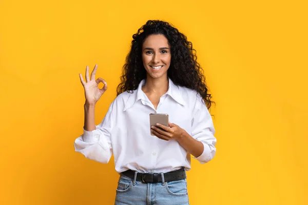 Grande offerta mobile. Sorridente giovane donna in possesso di smartphone e mostrando gesto ok — Foto Stock