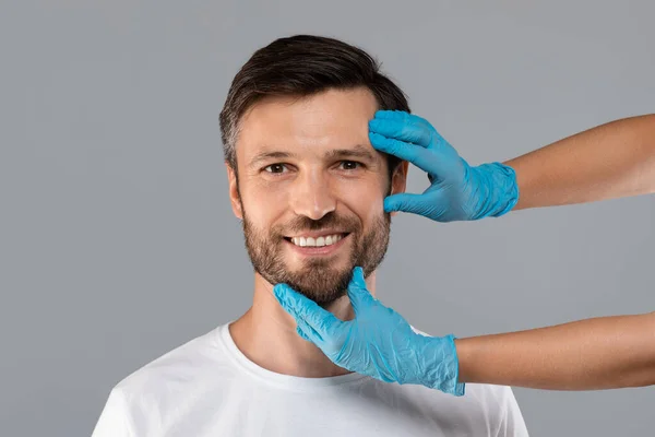 Cosmetician mãos em luvas de proteção tocando rosto homem sorridente — Fotografia de Stock