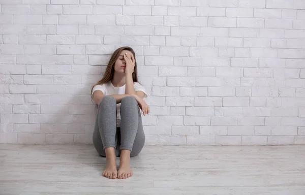 Yksinäinen nuori nainen istuu lattialla kotona, masentunut ja toivoton, kopioi tilaa — kuvapankkivalokuva