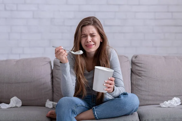 Comer emocionalmente. Mujer estresada llorando en el sofá con un cubo de helado, viendo una película triste y sintiéndose deprimida — Foto de Stock