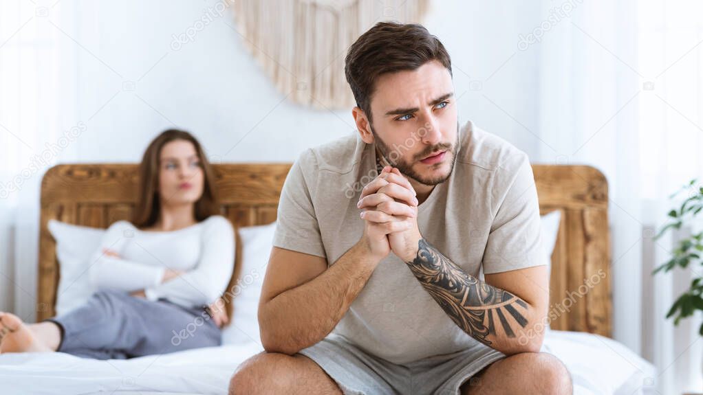Man and woman feeling stressed and angry at each other, sits on wooden bed and look to side of free space