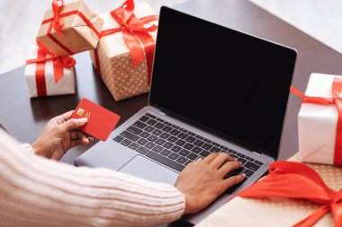 Evde dizüstü bilgisayar ve kredi kartı kullanan siyah bir kadın.