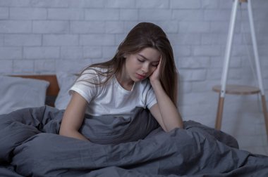 Kış depresyonu kavramı. Mevsimsel duygusal bozukluğu ya da depresyonu olan üzgün genç bir kadın yatağında yalnız başına oturuyor.