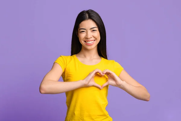 Freundliche asiatische Frau formt Hände wie Herzen und macht Liebesgeste in Brustnähe — Stockfoto