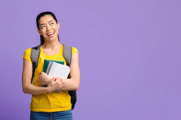 Dromerige Koreaanse vrouwelijke student met rugzak en werkboeken over paarse studio achtergrond — Stockfoto