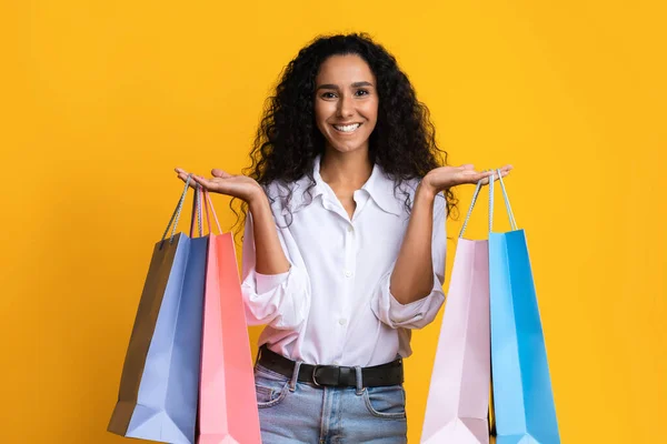 Mujer joven positiva con un montón de bolsas de compras posando sobre fondo amarillo — Foto de Stock