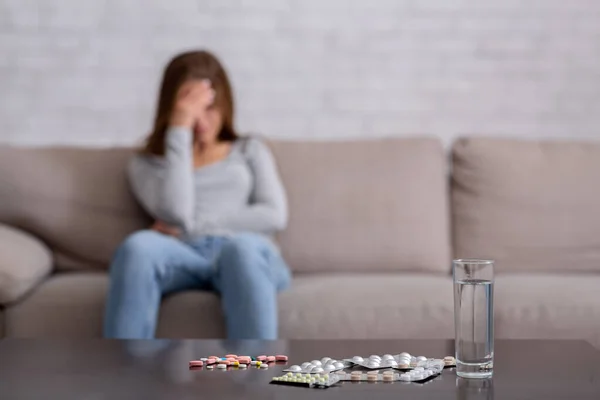 Αυτοκτονία από υπερβολική δόση φαρμάκων. Χάπια και νερό στο τραπέζι και καταθλιπτική νεαρή γυναίκα κλαίει στο παρασκήνιο, αντίγραφο χώρο — Φωτογραφία Αρχείου