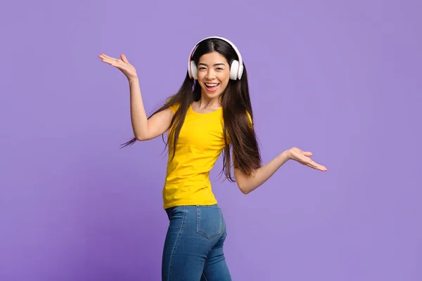 Alegre mujer asiática escuchando música en auriculares y bailando con las manos extendidas — Foto de Stock