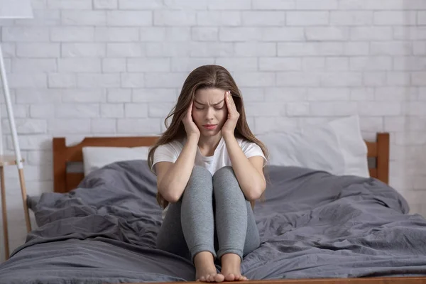 Unglückliche Millennial Lady sitzt auf dem Bett und massiert ihre Schläfen, hat Kopfschmerzen oder Depressionen — Stockfoto