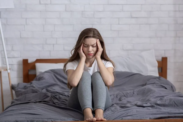 Olycklig tusenårig dam sitter på sängen och masserar sina tempel, har huvudvärk eller depression — Stockfoto