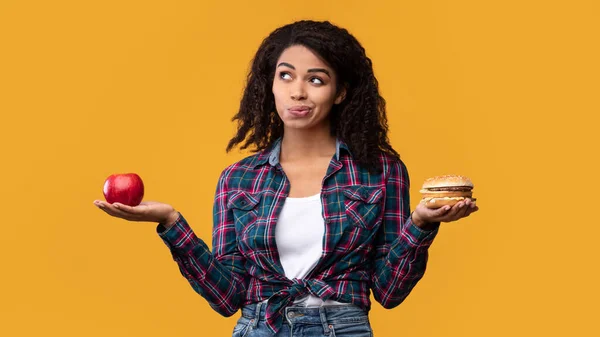 Hambre negro dama sosteniendo hamburguesa y manzana fruta — Foto de Stock