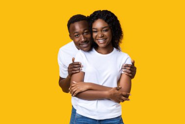 Siyah adam kız arkadaşına arkadan sarılıyor.