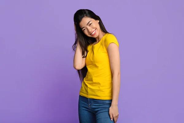 Estudio retrato de alegre asiática mujer tocando el pelo, posando sobre púrpura fondo — Foto de Stock