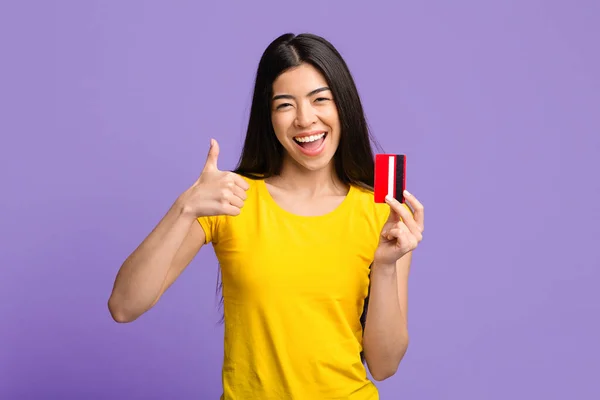 Emocionado alegre asiática mujer celebración de tarjeta de crédito y mostrando pulgar hacia arriba — Foto de Stock