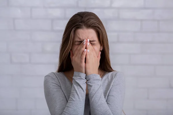 Deprimida mujer milenaria cubriendo su cara y llorando contra la pared de ladrillo blanco —  Fotos de Stock