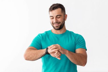 Mutlu Avrupalı atlet üniformalı atlet oturma odasının iç tarafındaki fitness izleyicisinin nabzını kontrol ediyor. Spor aleti, fitness, evde antrenman, covid-19 için kardiyo eğitimi