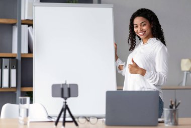 Modern öğretmen öğrenciler, webinar, eğitim ve yeni normaller için sanal ders veriyor. Mutlu Afro-Amerikan kadın öğretmen baş parmağını karatahtanın yanına kaldırdı, evdeki telefon kameralarına bak.