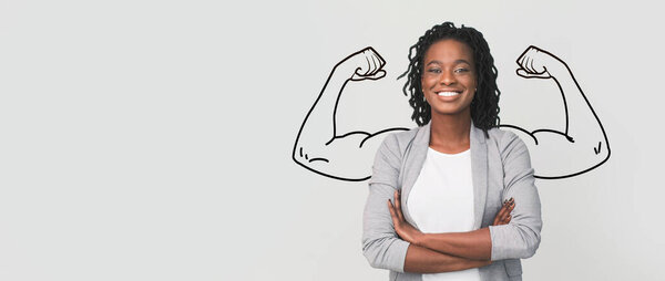 A strong African American woman stands proudly with crossed arms in a confident pose. The background is a soft panorama, emphasizing their biceps and determination in a moment of empowerment.