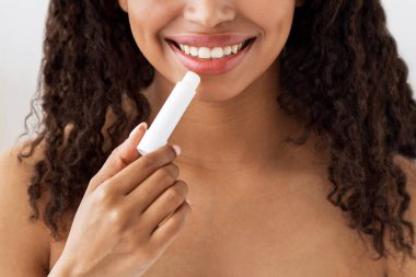 Makyajsız doğal güzelliğe sahip bir kadın evde cildi nemlendirir. Mutlu yüzyılın yakın portresi oldukça çıplak Afrikalı Amerikalı bir kadın beyaz yatak odasının iç kısmında dudaklarına ruj sürüyor.