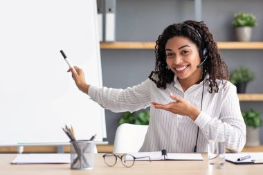 Sanal sınıfla çevrimiçi ders, evdeki öğrencilerle görüntülü konuşma ve yakınlaştırma konferansı, yeni normal. Dost canlısı siyah kulaklıklı bayan öğretmen tahtayı işaret ediyor, evdeki webcam 'e bakıyor.