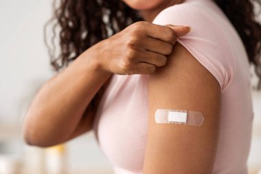 Virüs koruması, COVID-19 aşısı. Mutlu, genç, güzel, Afro-Amerikalı bir kadın modern mutfak içlerinde aşı olduktan sonra kollarını yara bandıyla gösteriyor.