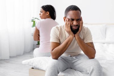 Unhappy offended young african american husband ignores wife, sit on comfortable bed back to back in bedroom interior. Conflict, scandal, quarrel at home, divorce and breakup during COVID-19 lockdown