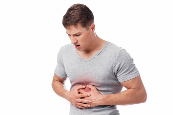 Unhappy young european male suffering from stomach pain, pressing hand to body, isolated on white background, copy space. Ache, heartburn, chronic gastritis or abdomen bloating and health problem